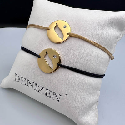 Two DENIZEN gold bracelets with an Aruba map cutout and a small CZ on beige and black strings