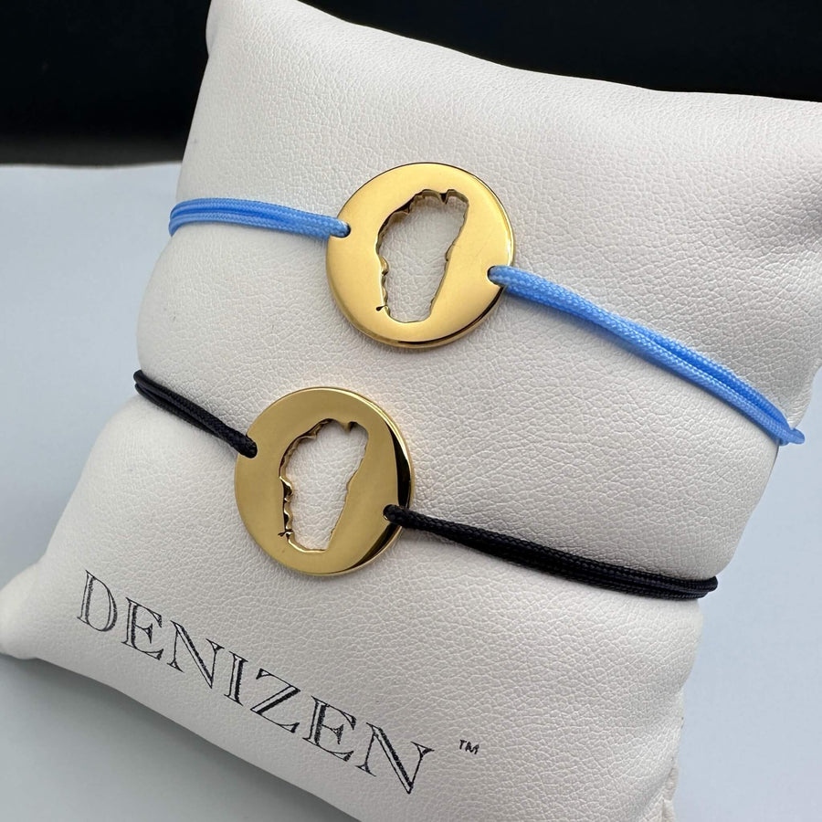 Two bracelets with rose gold circular medallions with Lake Tahoe cutouts and blue and black strings on a Denizen pillow.
