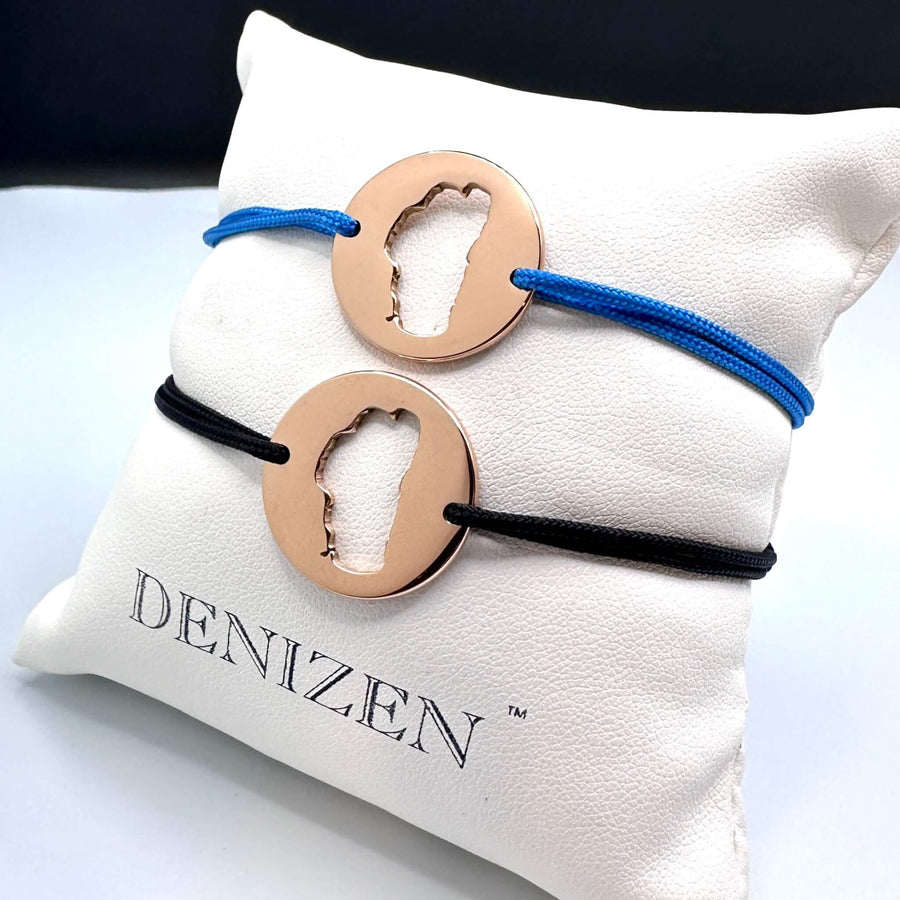 Two bracelets with rose gold circular medallions with Lake Tahoe cutouts and blue and black strings on a Denizen pillow.