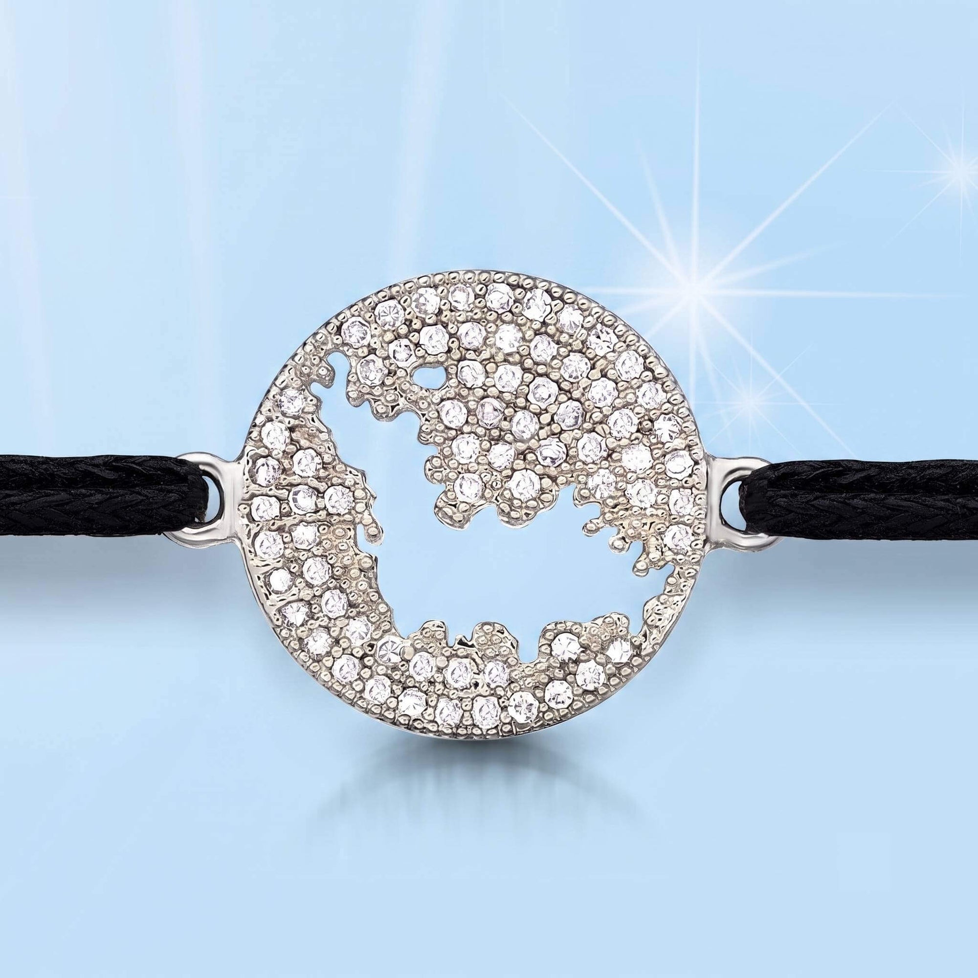 A round silver bracelet featuring a cutout of  the map of St Barth, embellished with clear pavé rhinestones, attached to a black braided cord.