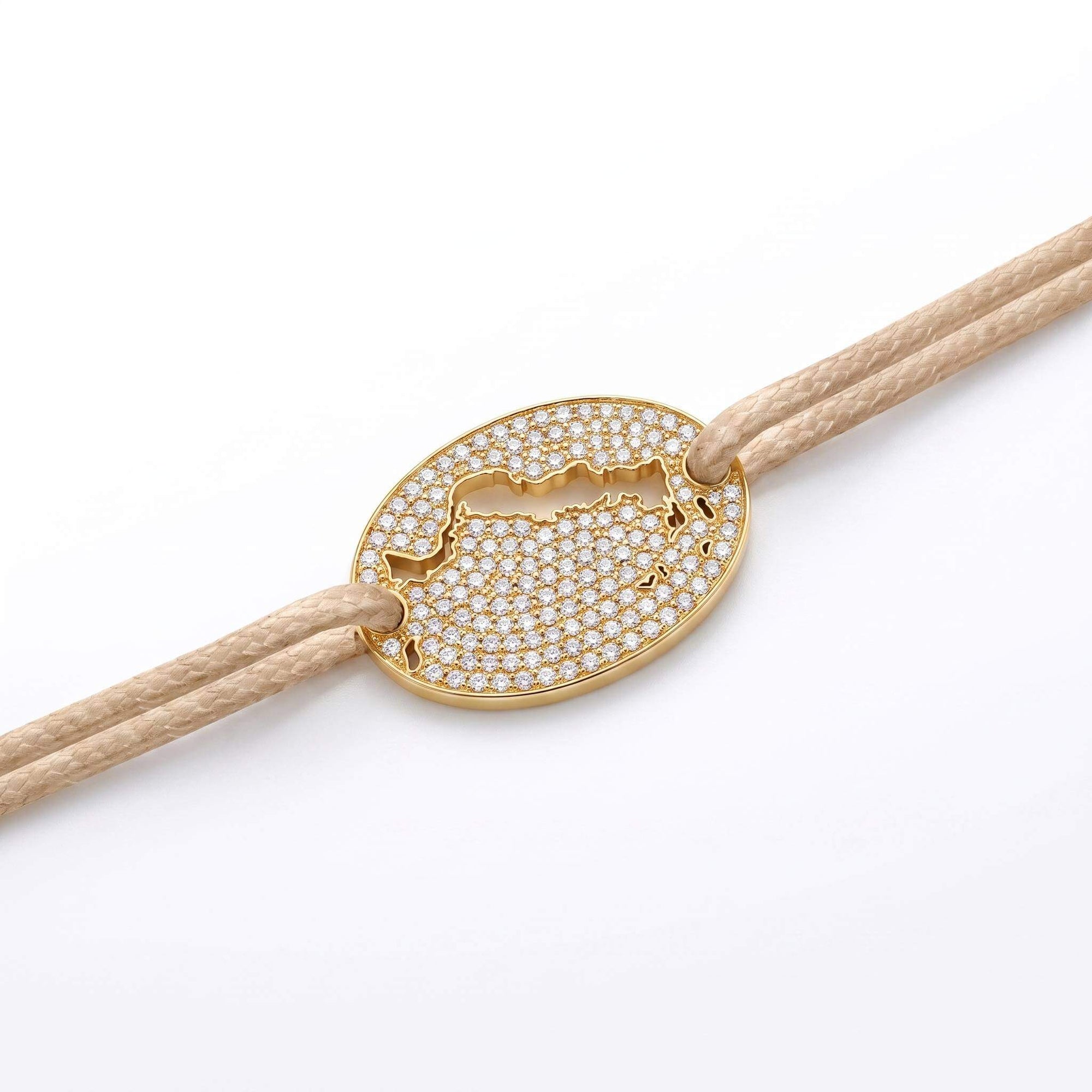 A gold oval bracelet featuring a cutout of the Turks and Caicos map paved with small clear stones, threaded on a beige cord against a white background.