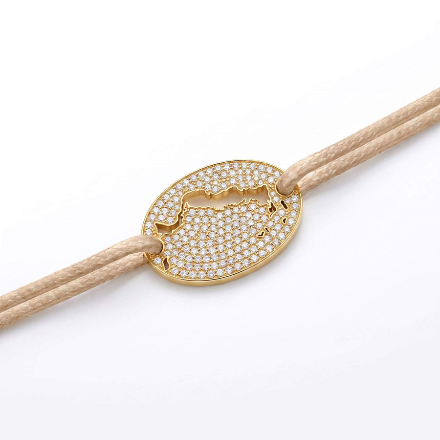 A gold oval bracelet featuring a cutout of the Turks and Caicos map paved with small clear stones, threaded on a beige cord against a white background.