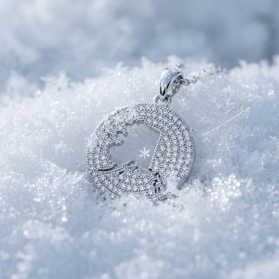 A round gold pendant necklace pavé-set design, displayed on snow with scattered gold nuggets. The pendant features a central cutout of the Alaska map.