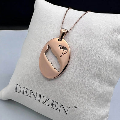 A DENIZEN rose gold oval pendant on a chain with a cutout map of Aruba and a small flamingo