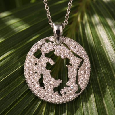 A silver pendant necklace with a cutout map of Bora Bora in a diamond pavé, resting on palm leaf.