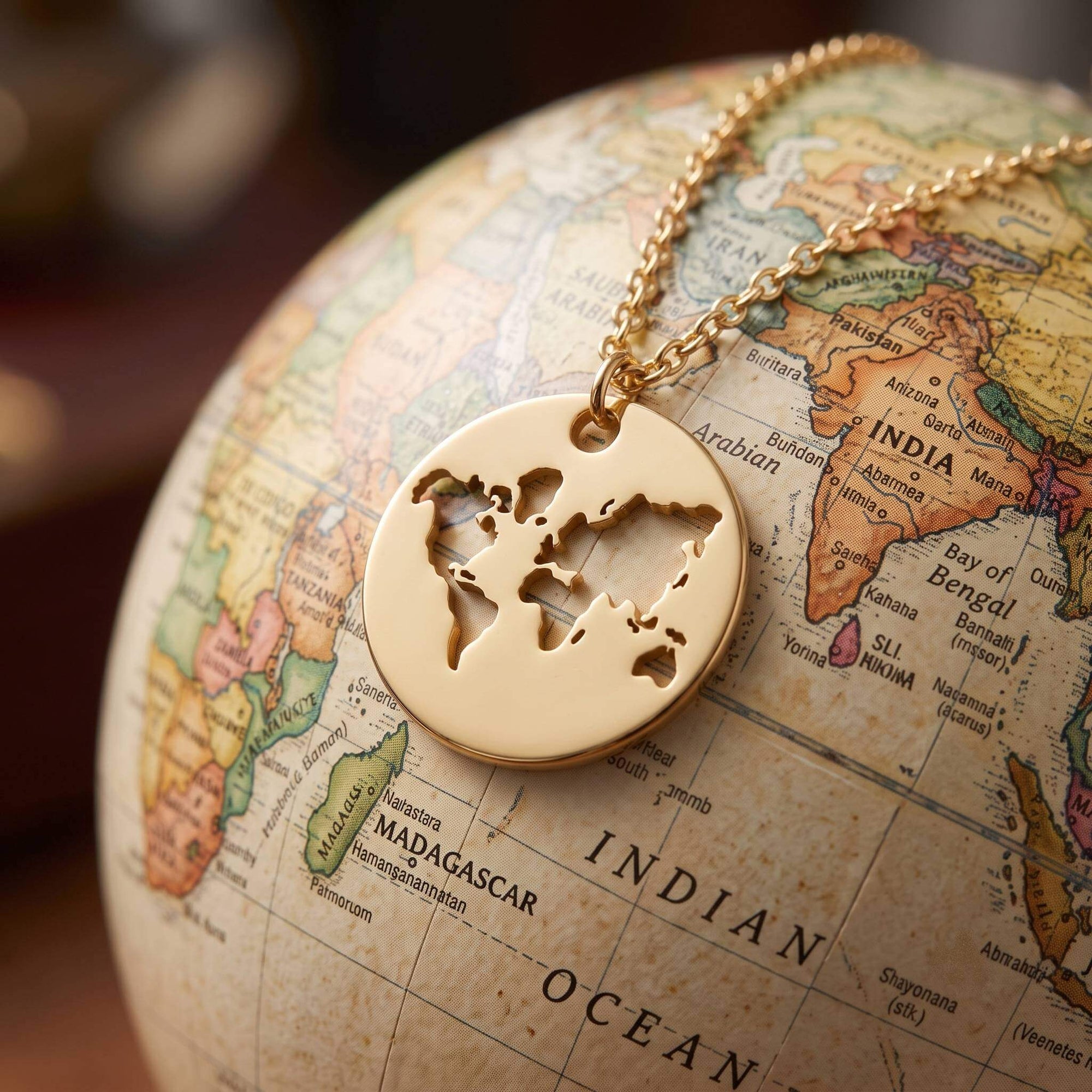 A gold round pendant necklace with a cutout world map design, resting on a vintage-style globe map.