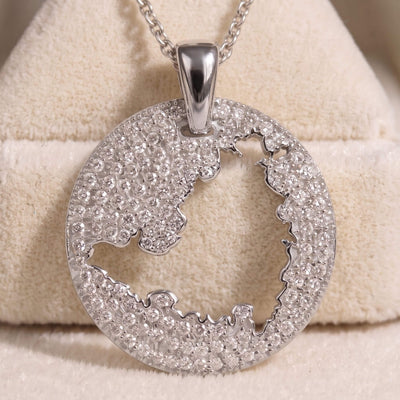 A silver-toned oval pendant necklace paved with clear stones, featuring a cut-out map of St. Maarten, displayed on a beige textured jewelry stand.
